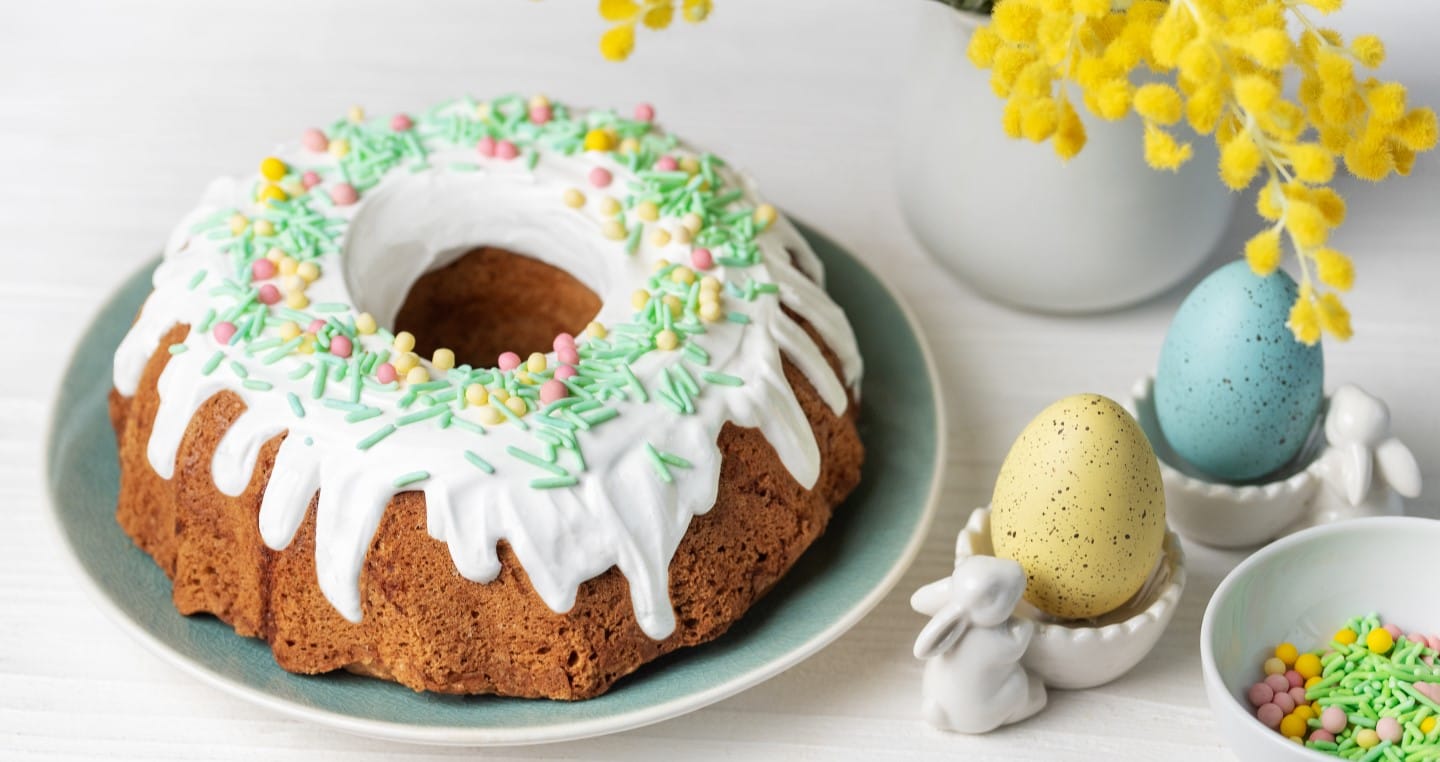 babka wielkanocna z polewą i posypką, obok dwa kolorowe jajka wielkanocne i króliczek