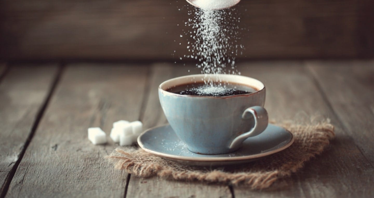 Dodawanie cukru do filiżanki kawy na drewnianym stole.