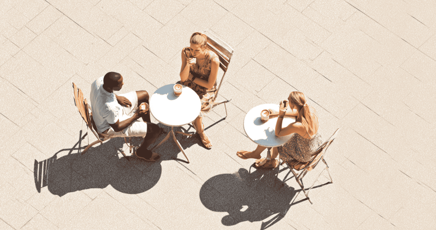 Trzy osoby pijące kawę na zewnątrz, siedzące przy dwóch stolikach.