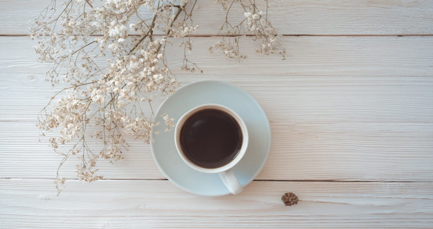 Filiżanka czarnej kawy na białym stole obok gałązki białych kwiatów.