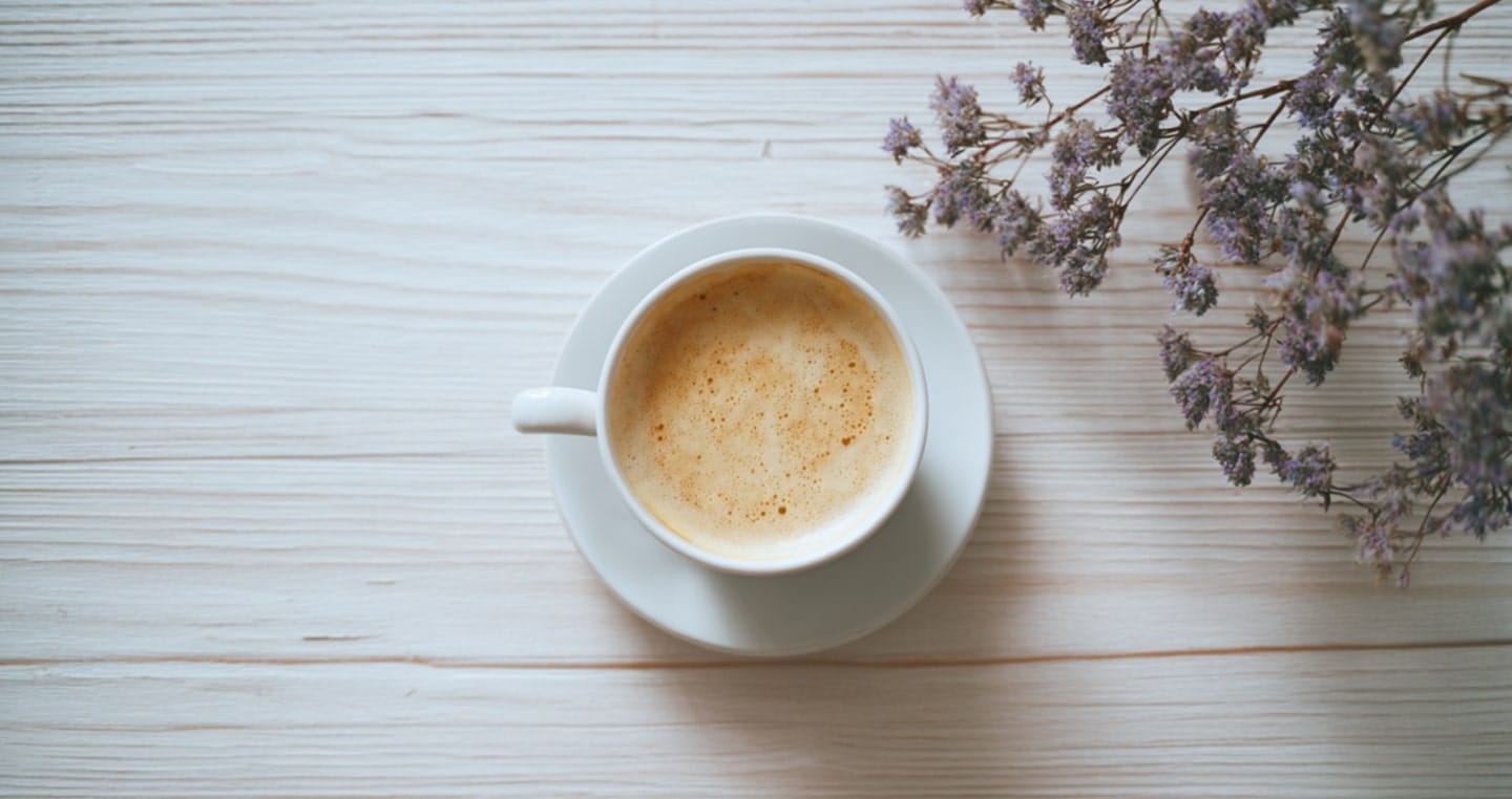 Filiżanka kawy na białym talerzyku, obok gałązka lawendy.