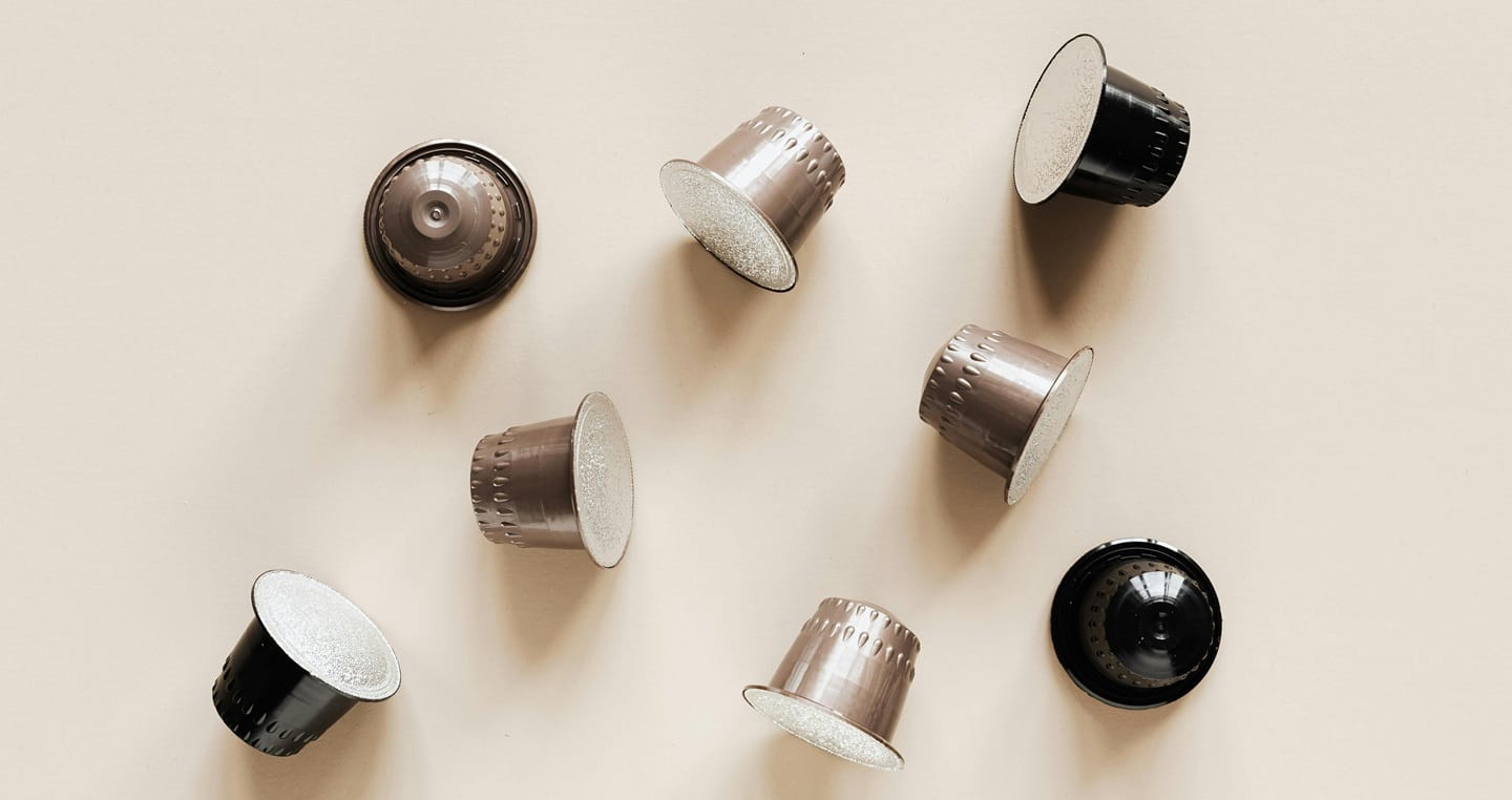 Osiem kapsułek do kawy w kolorach czarnym i brązowym na jasnym tle.