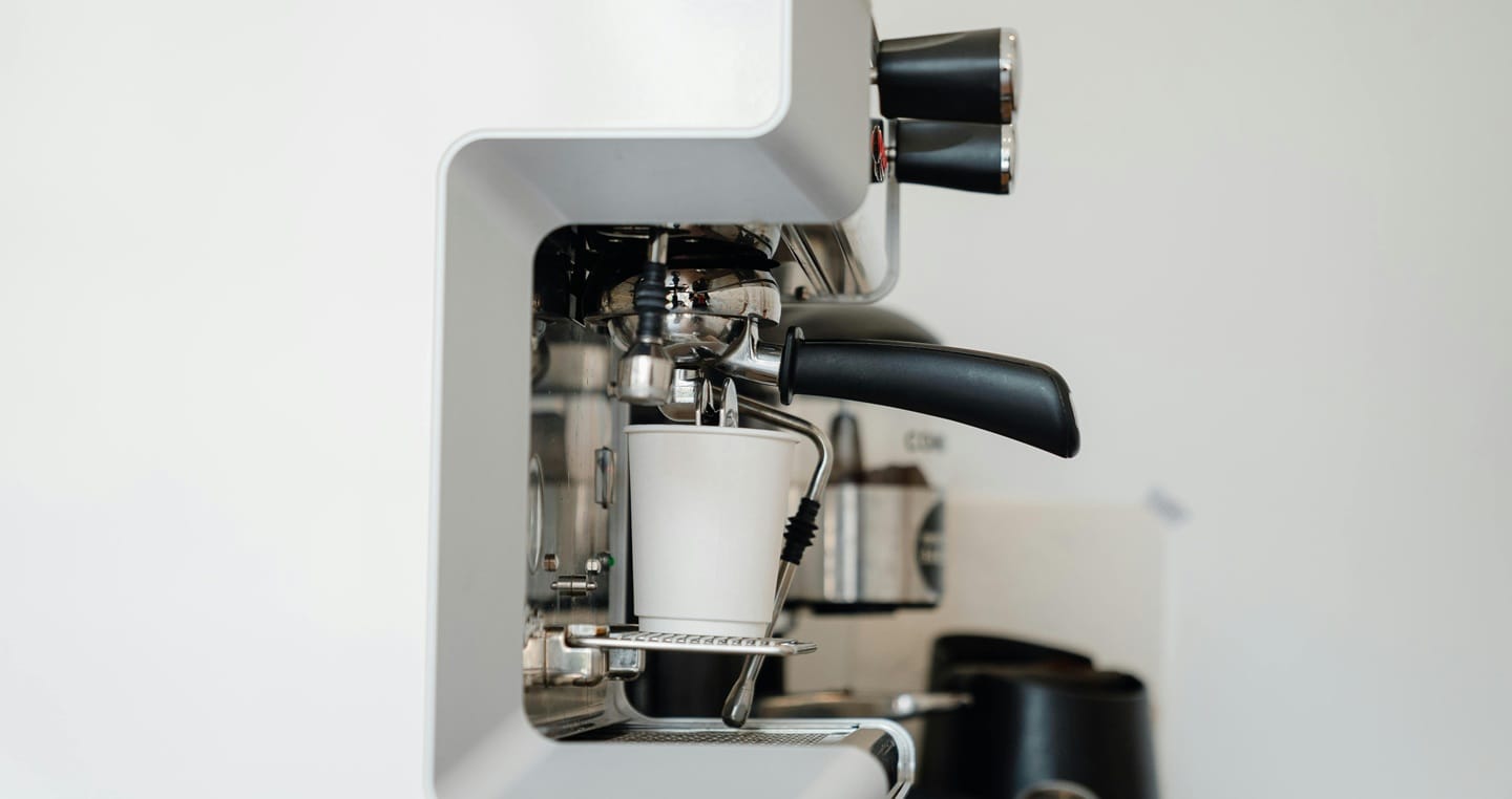 Ekspres do kawy przygotowuje napój w białym kubku.