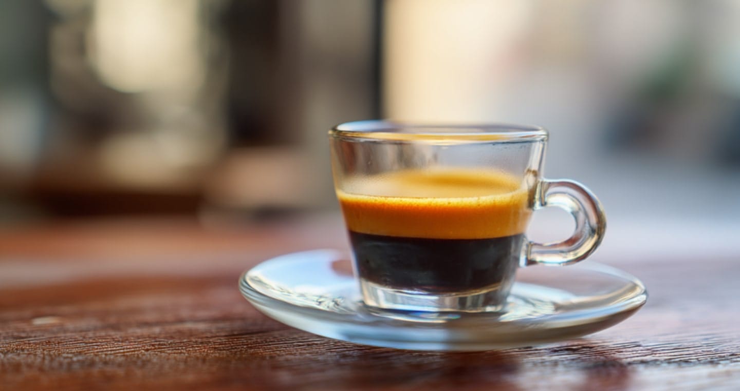 Filiżanka espresso coretto na drewnianym stole, rozmyte tło.