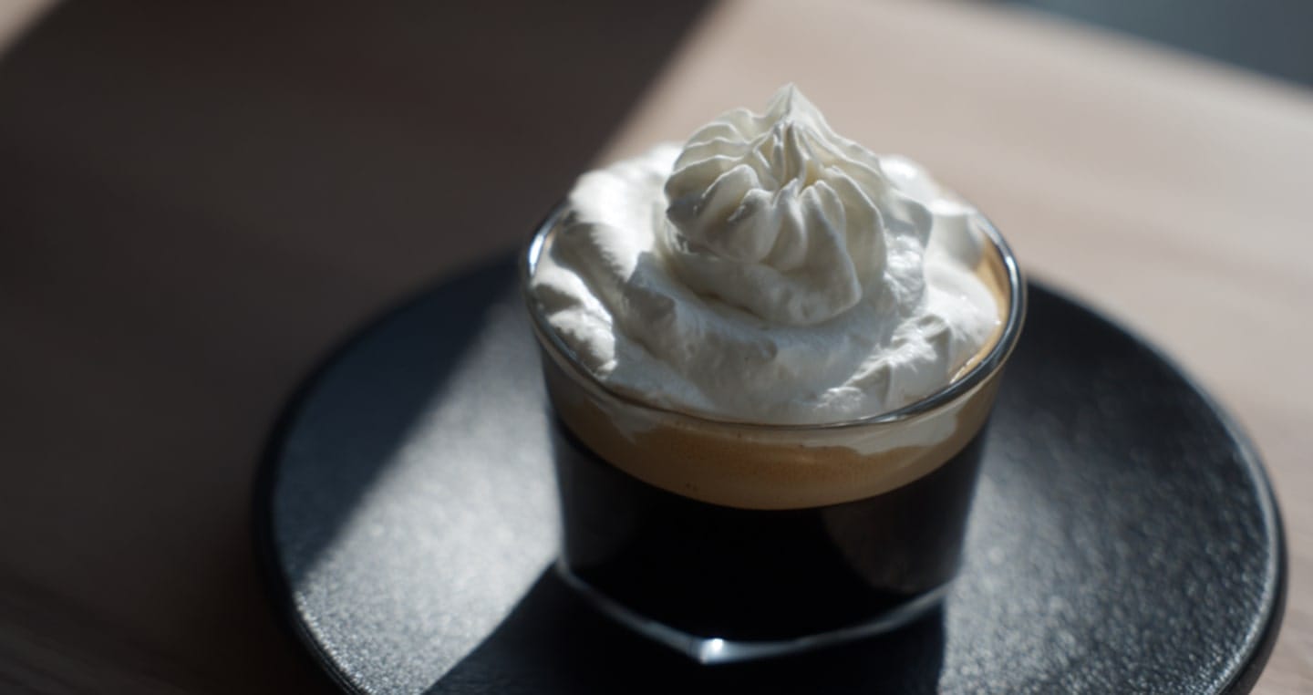 Kubek kawy espresso con Panna z bitą śmietaną na ciemnym talerzu.