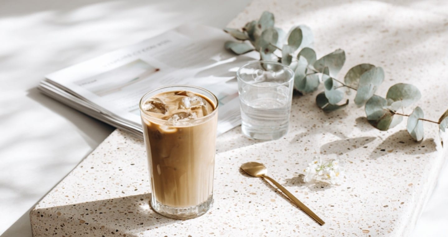 Kawa jęczmienna, szklanka wody, złota łyżeczka, magazyn, gałązka eukaliptusa.