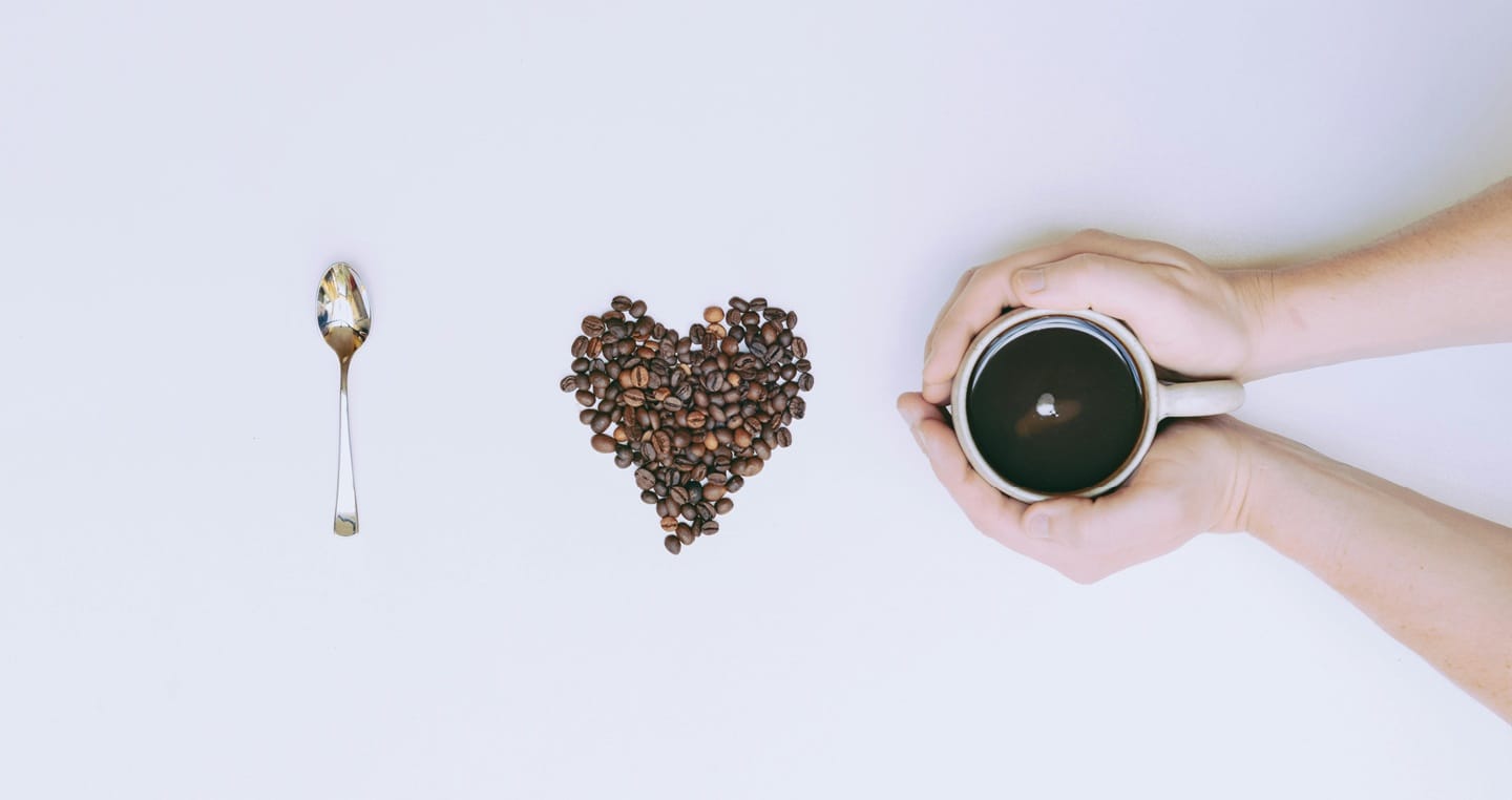 Łyżka, serce z ziaren kawy, dłonie trzymające filiżankę kawy zmierzonej przez refraktometr .