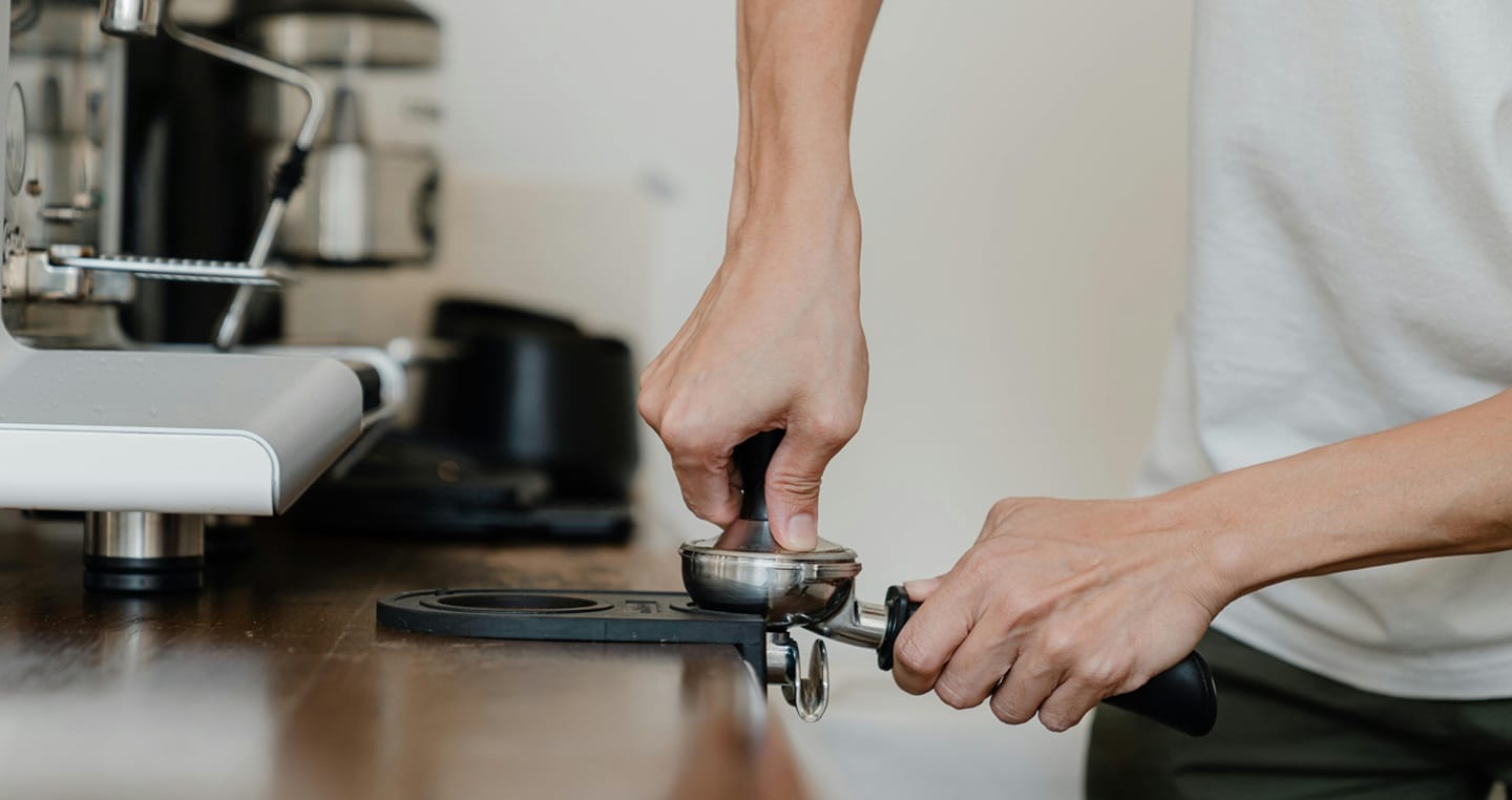 Tamper do kawy i osoba ubija kawę w kolbie przy ekspresie do kawy.