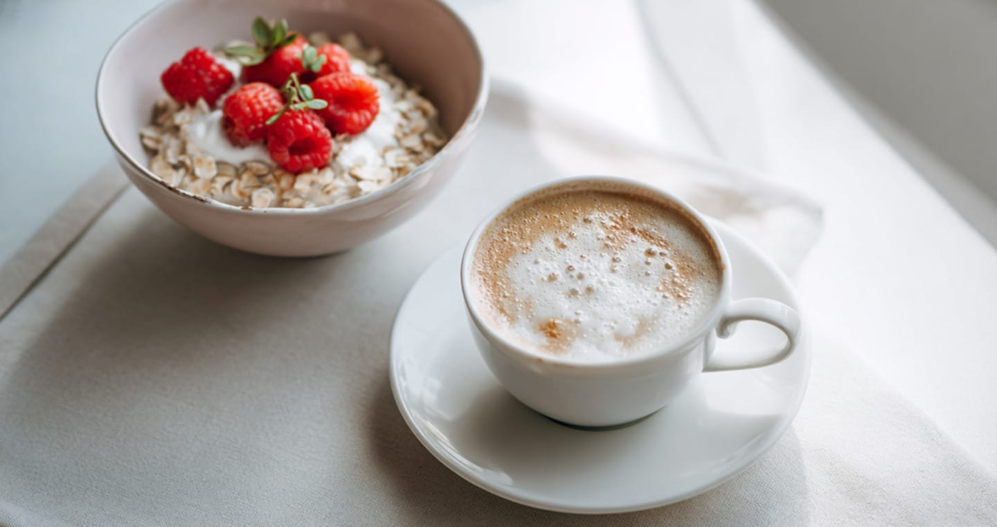 Białe tło, biała miska z truskawkami i smakowe cappuccino w białej filiżance.