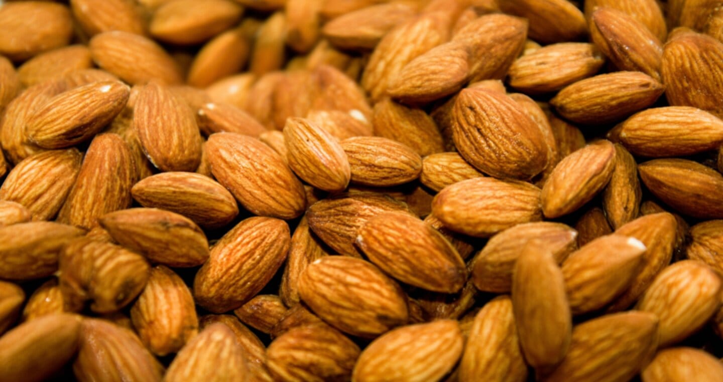 Brązowe migdały w skórce, ułożone w stos.