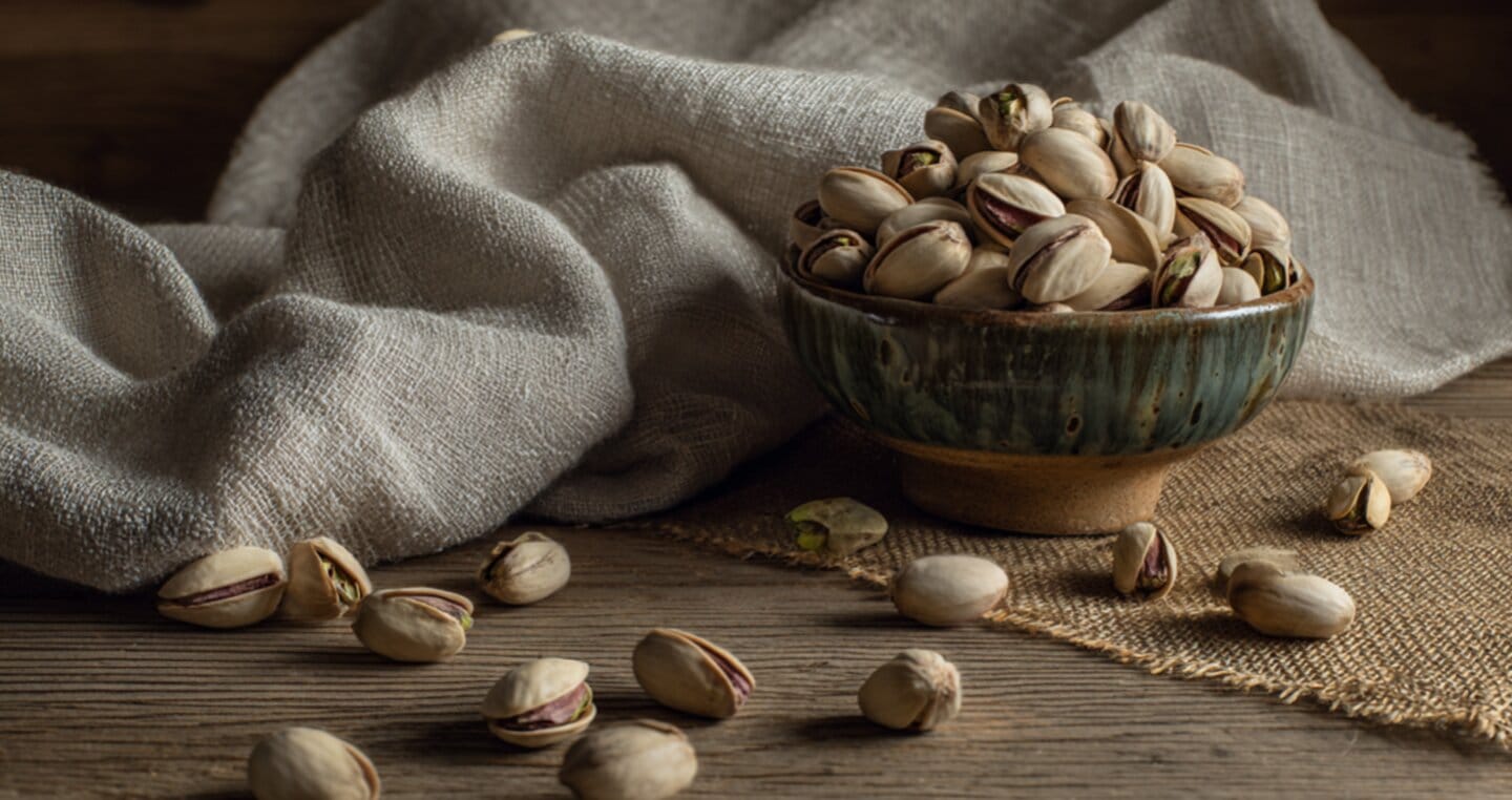 Miseczka pełna pistacji na drewnianym stole, z lnianą tkaniną w tle.