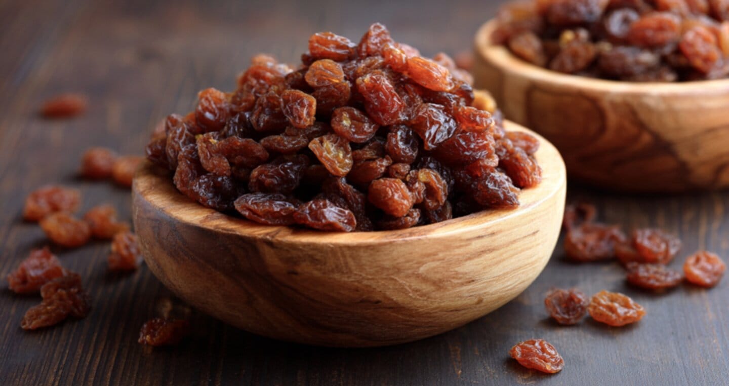 Dwie drewniane miski wypełnione suszonymi rodzynkami na ciemnym tle.