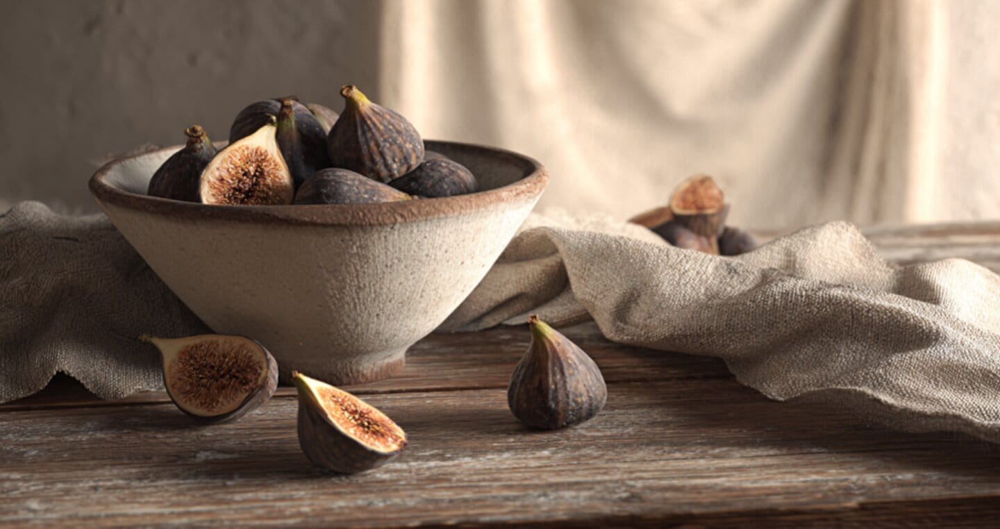 Miseczka pełna fig na drewnianym stole, obok szmatka i pokrojone figi.