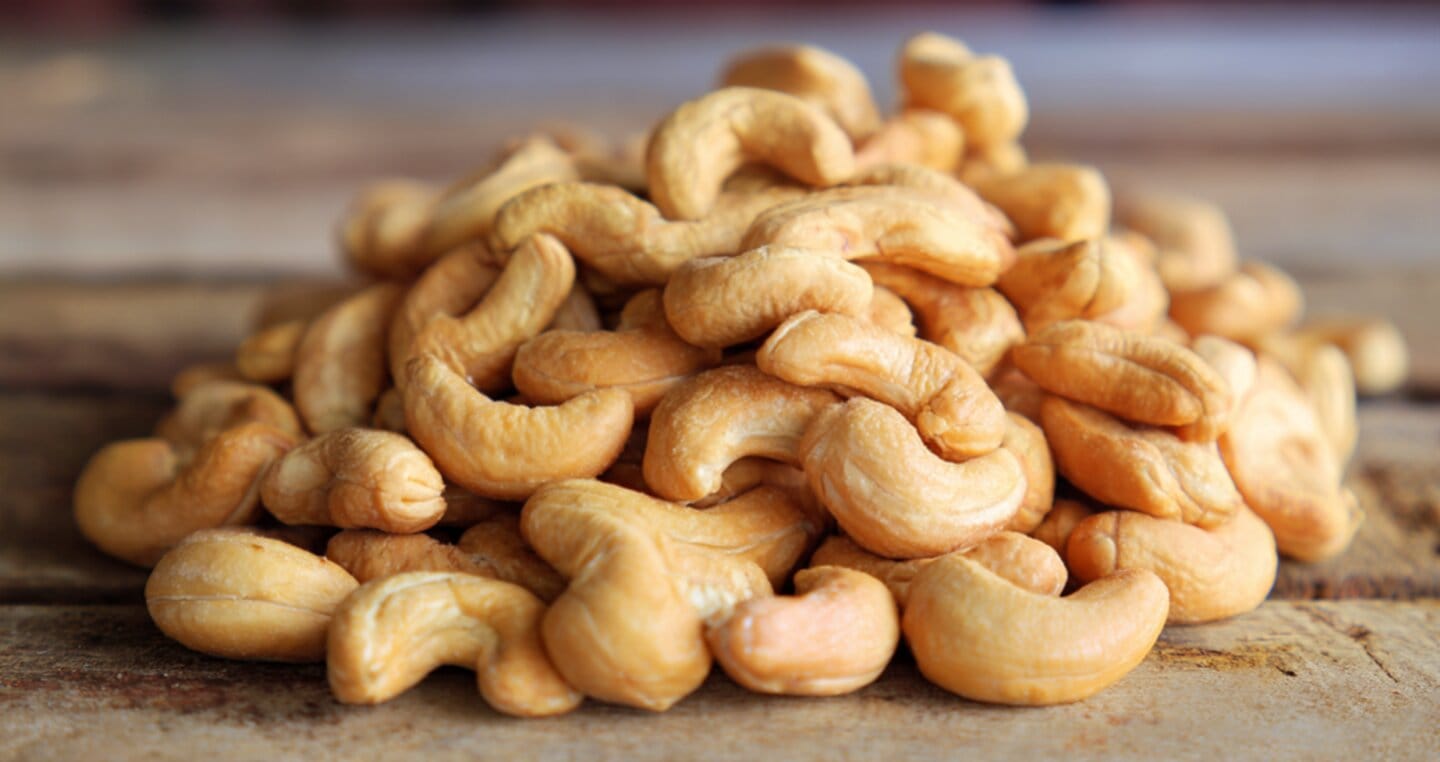 Orzechy nerkowca usypane w stos na drewnianej desce.