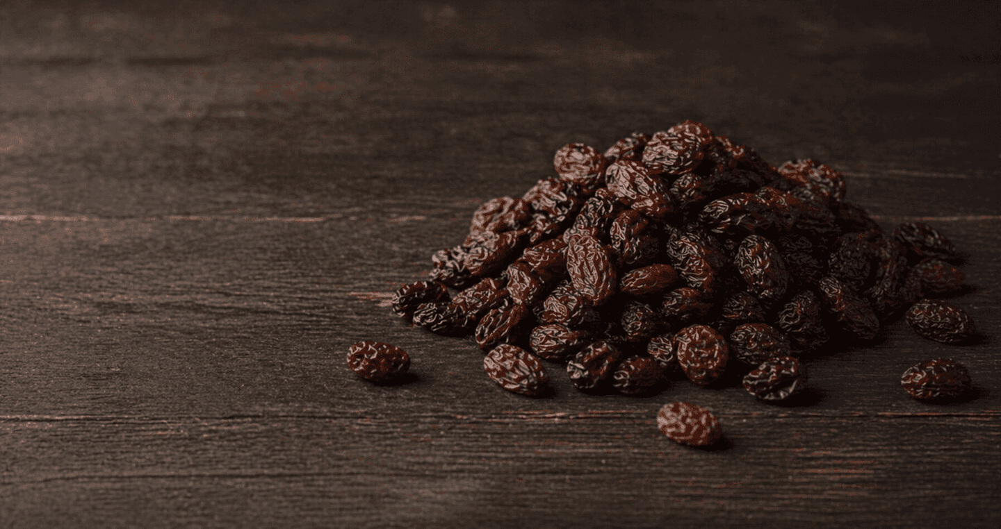 Niewielka porcja rodzynek na ciemnym drewnianym blacie.