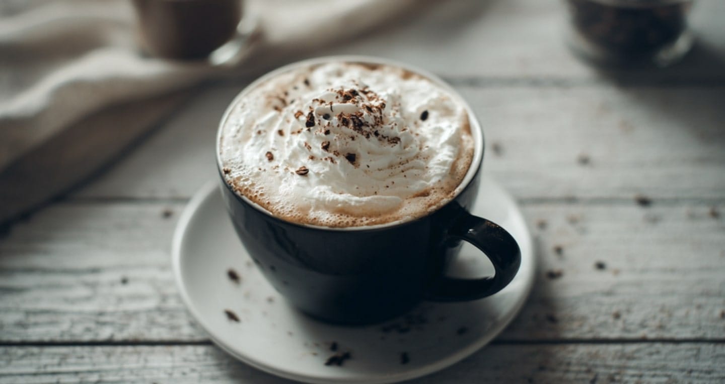 kawa z bitą śmietaną w niebieskiej filiżance z białym spodkiem na szarym stole