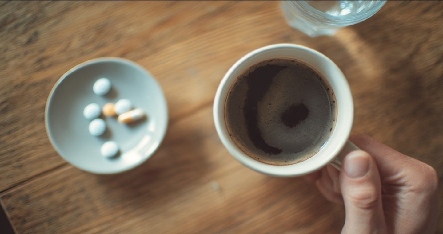 kubek kawy i talerzyk z różnokolorowymi tabletkami na brązowym stole