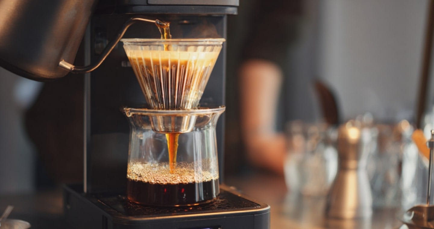 Krople gorącej kawy spływają przez filtr do szklanego dzbanka.