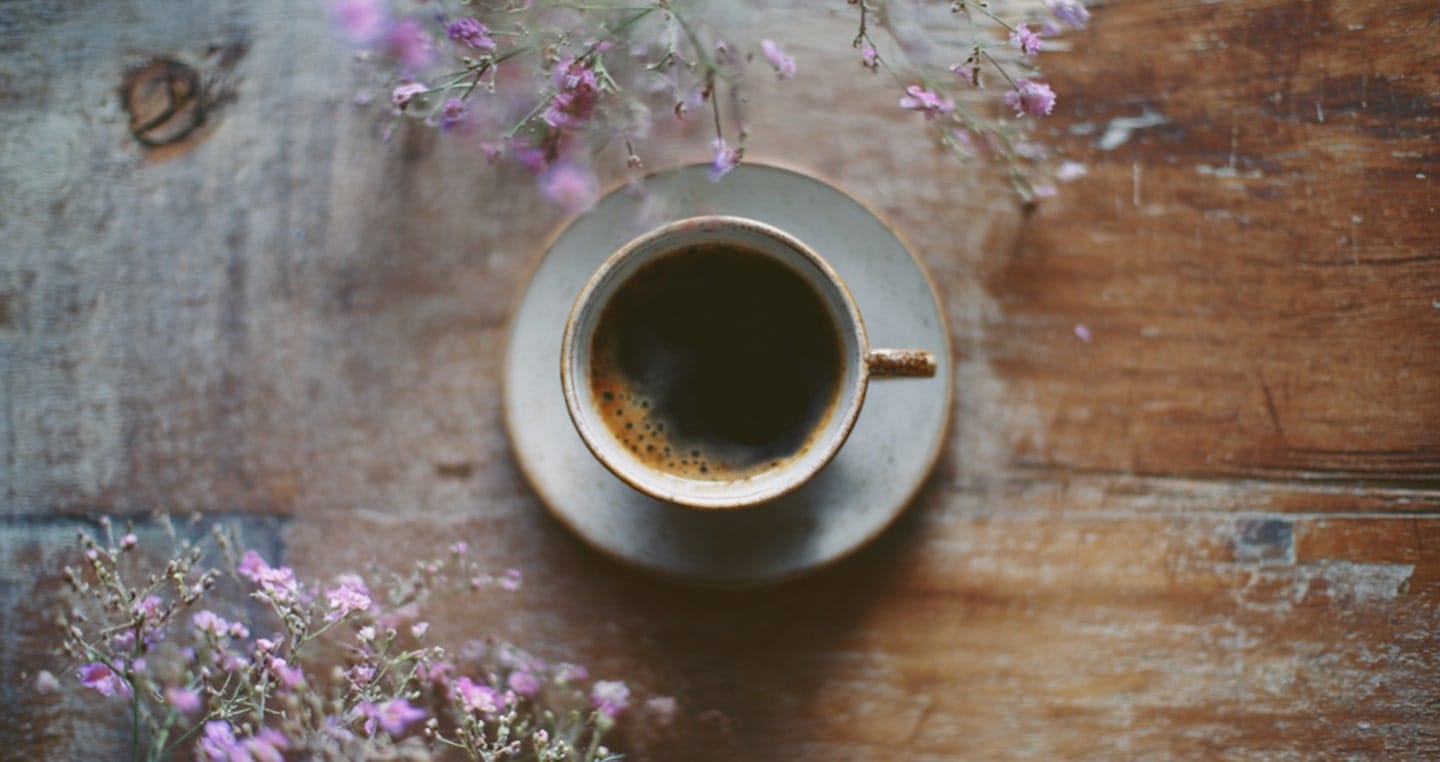 Filiżanka czarnej kawy na drewnianym stole z różowymi kwiatami.