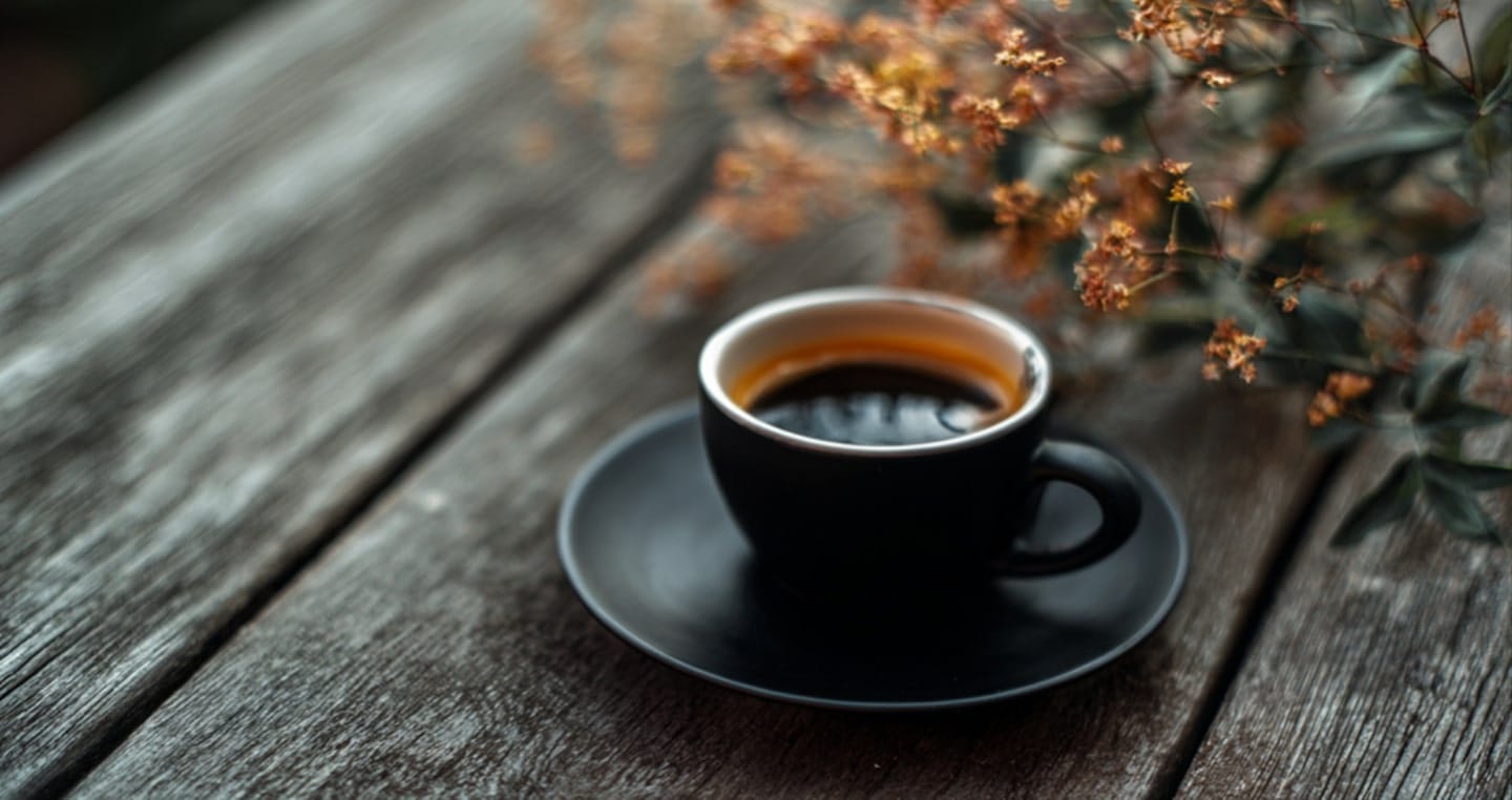 Czarna filiżanka espresso na drewnianym stole, obok gałązki kwiatów.