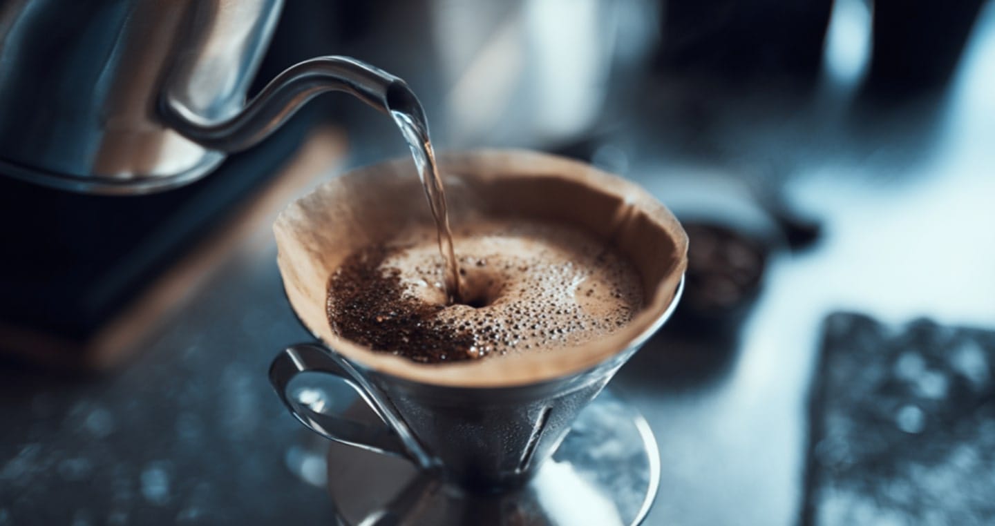 Parzenie kawy metodą przelewową w stalowym dzbanku, widoczny filtr z kawą.