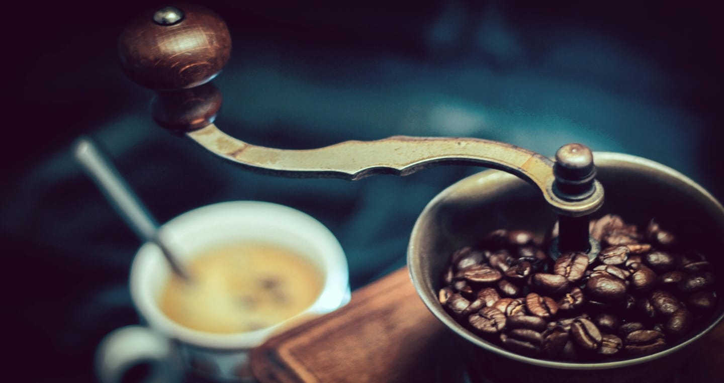 Ręczny młynek do kawy i filiżanka z kawą na ciemnym tle.