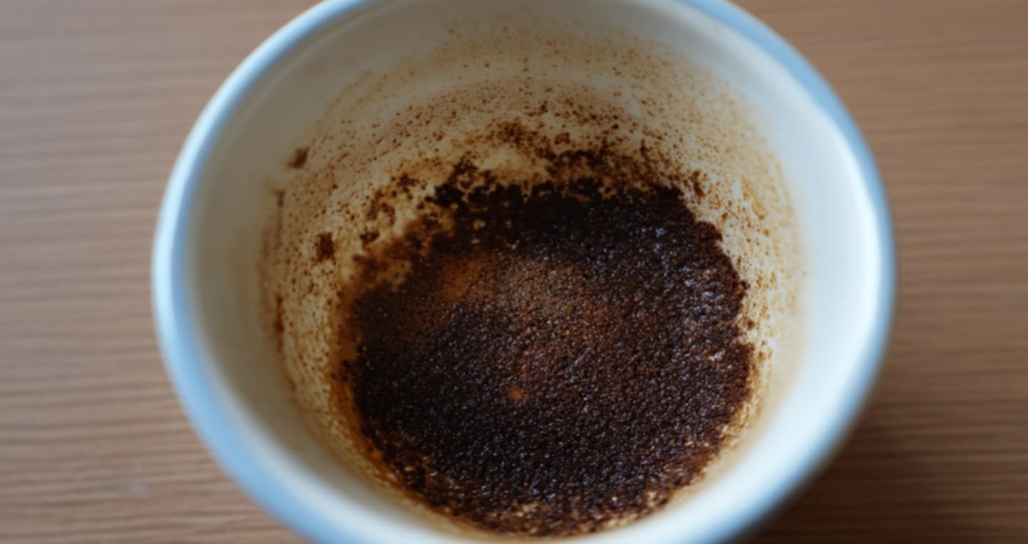 Fusy kawy na dnie białej filiżanki, drewniane tło.