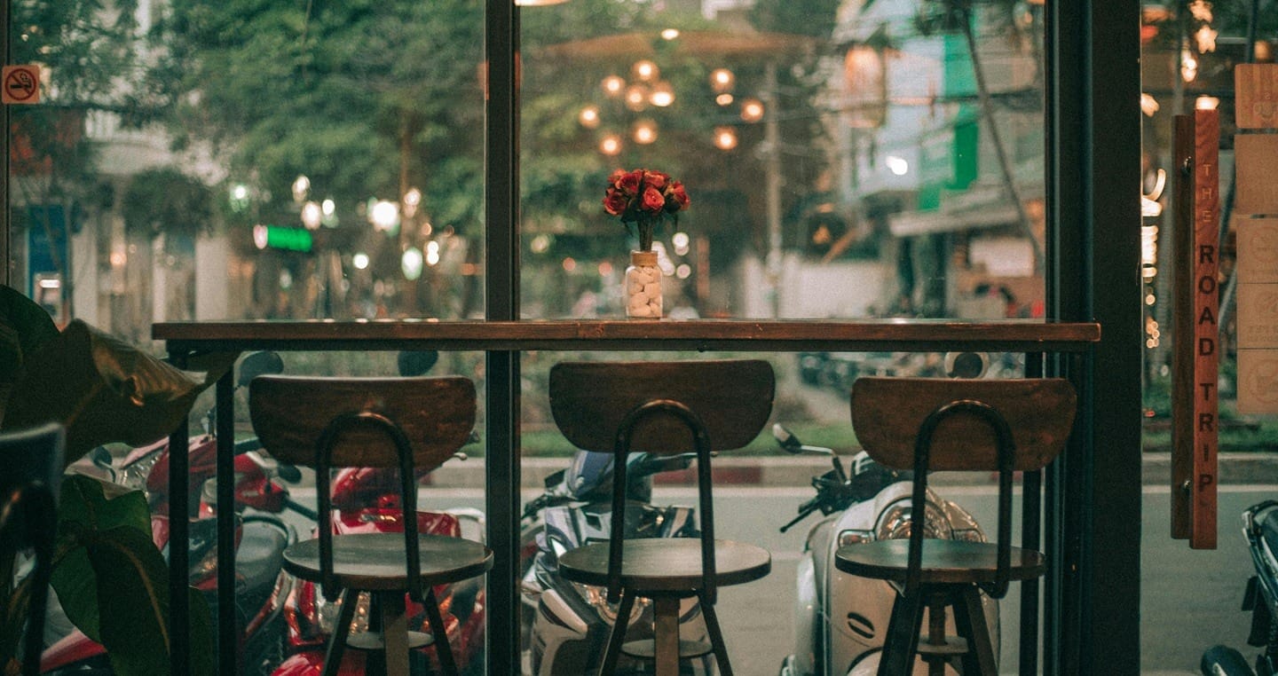 Stolik z trzema krzesłami, wazonem z różami, widok na ulicę.