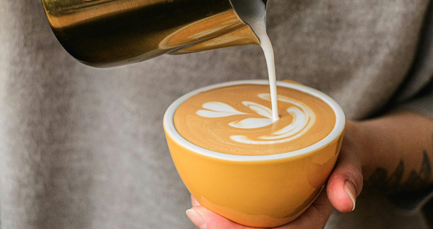 Nalewanie mleka do kawy z odchodów nietoperza, wzór latte art w żółtej filiżance.