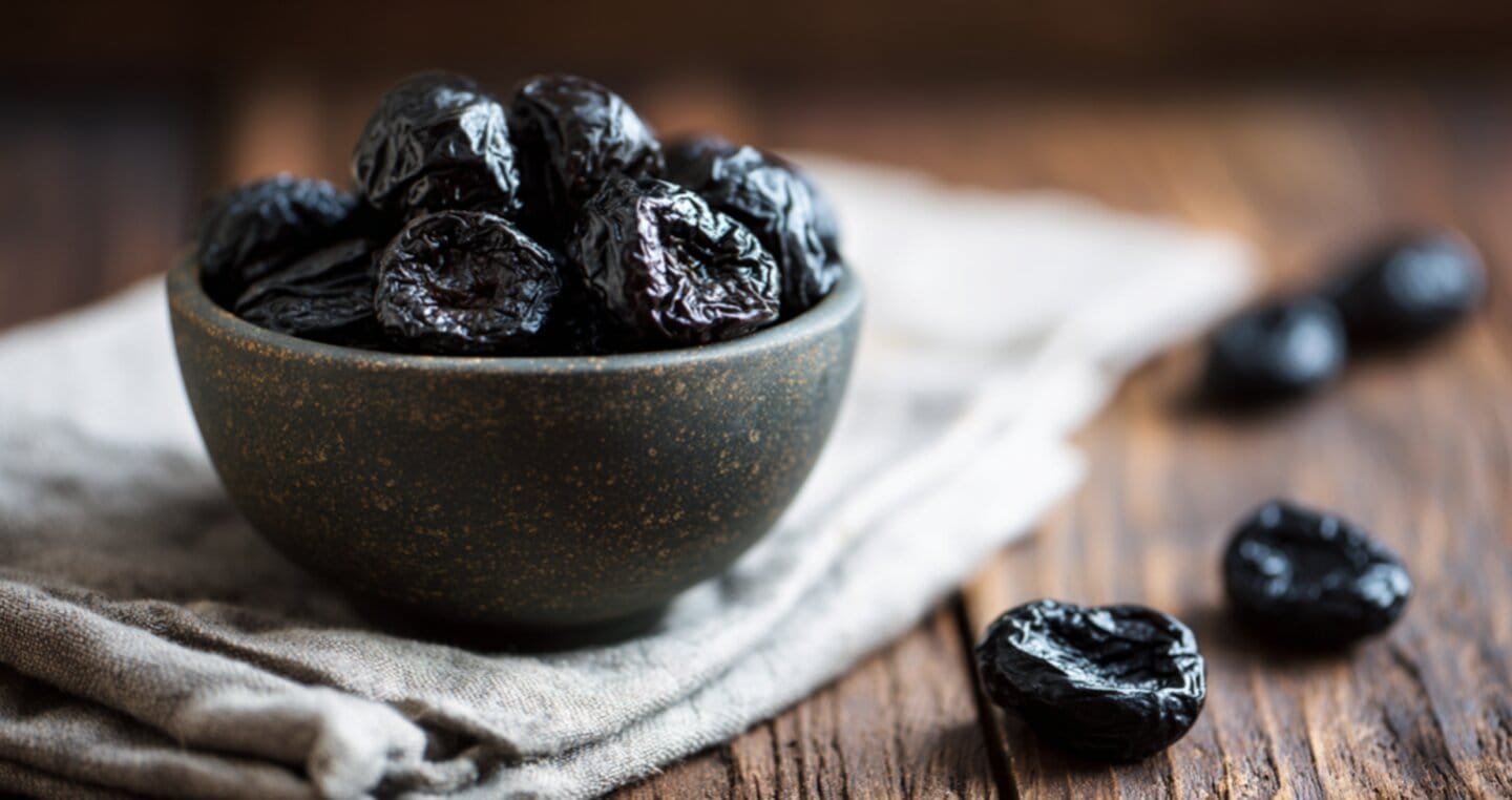 Suszone śliwki w misce na drewnianym stole, niektóre poza miską.