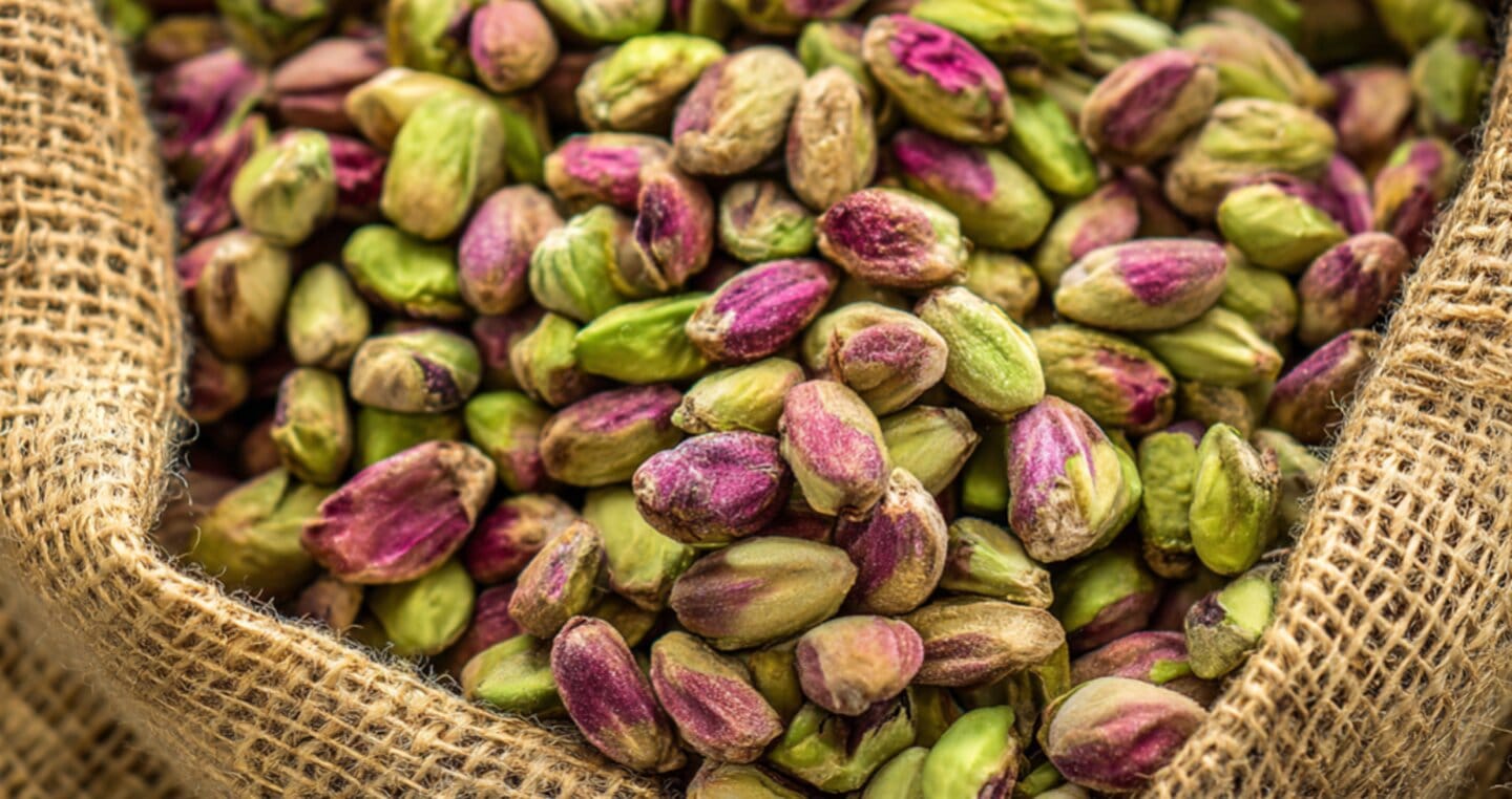 Pistacje w jutowym worku, zielone i fioletowe nasiona.