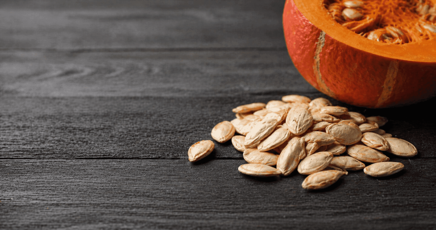 Pestki dyni Hokkaido obok przekrojonej pomarańczowej dyni na ciemnym drewnianym blacie